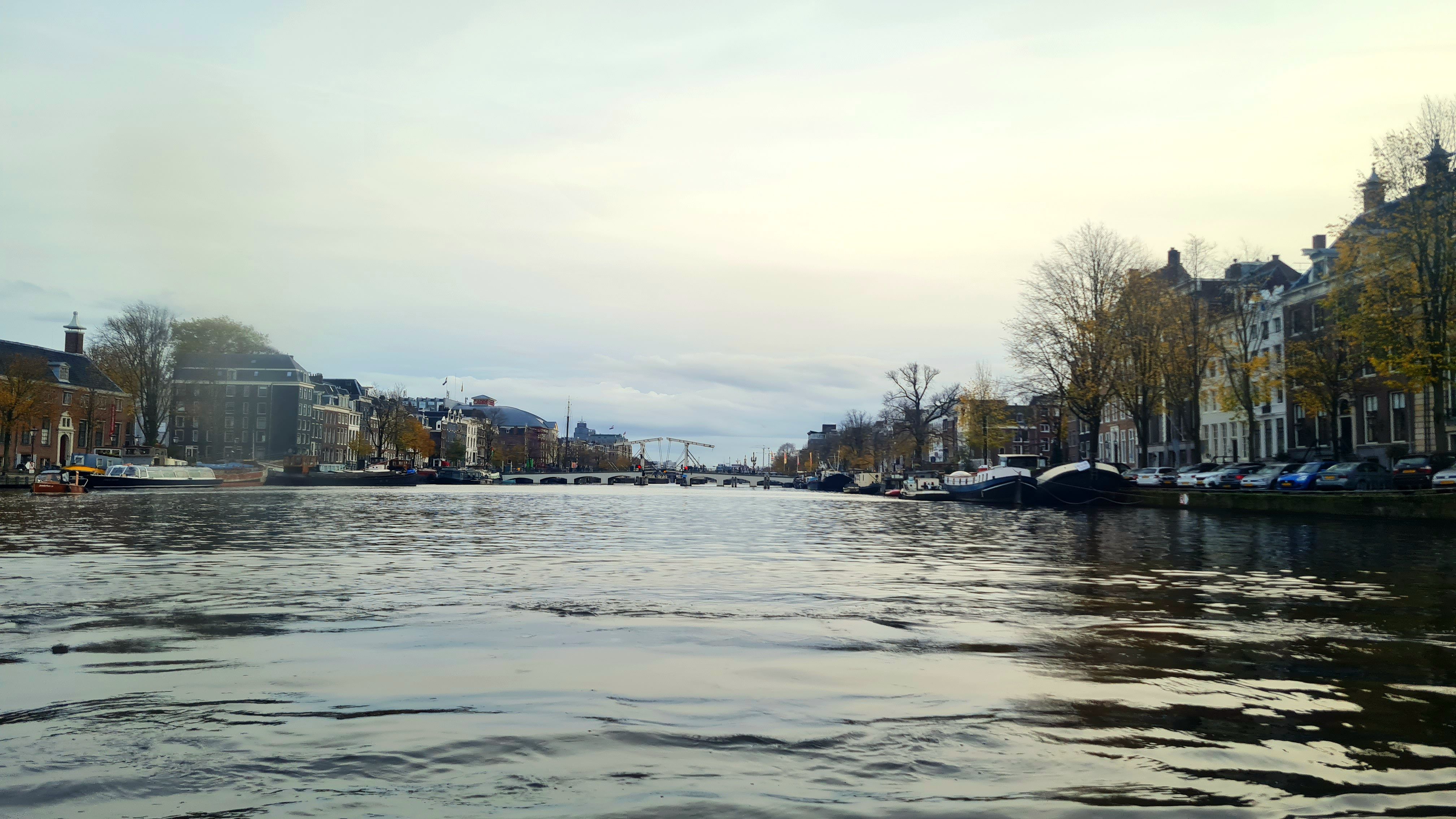 The Amstel river seen from water level, with houseboats on the right and a white drawbridge in the distance, Amsterdam