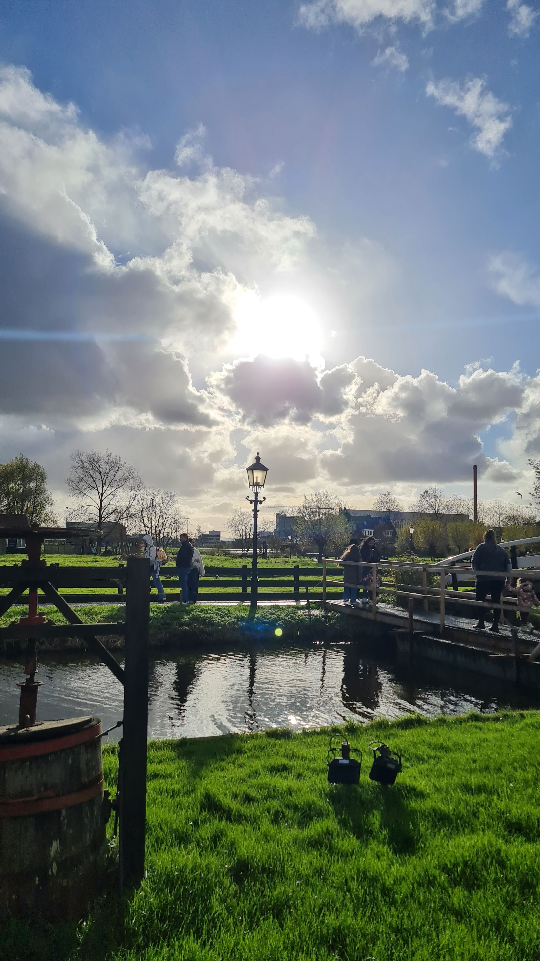 The sun breaking through clouds behind a lamp post and a small white footbridge over a canal, Zaanse Schans