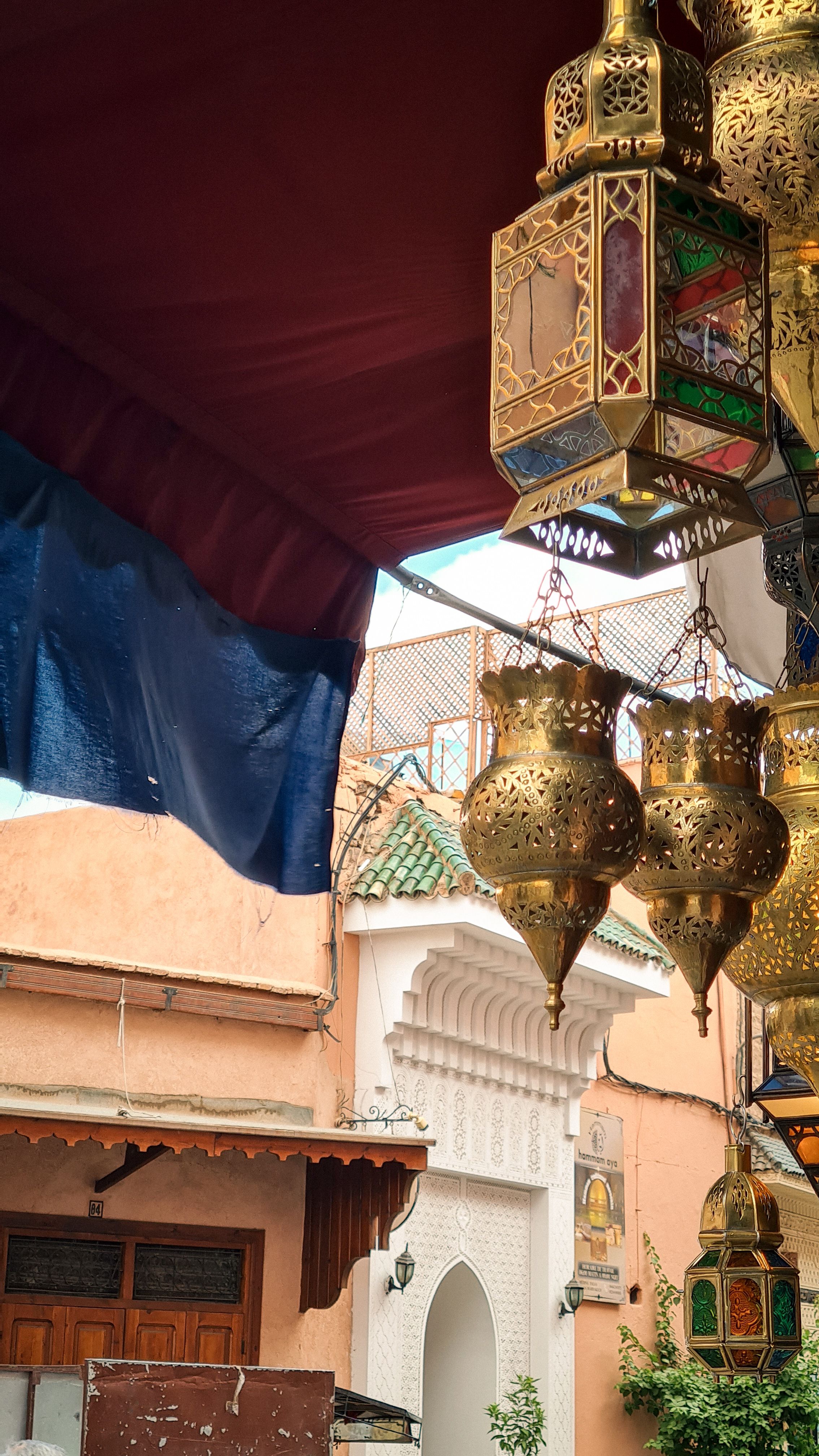 Pierced brass lanterns hanging beneath a red awning above a pink medina courtyard, Marrakech