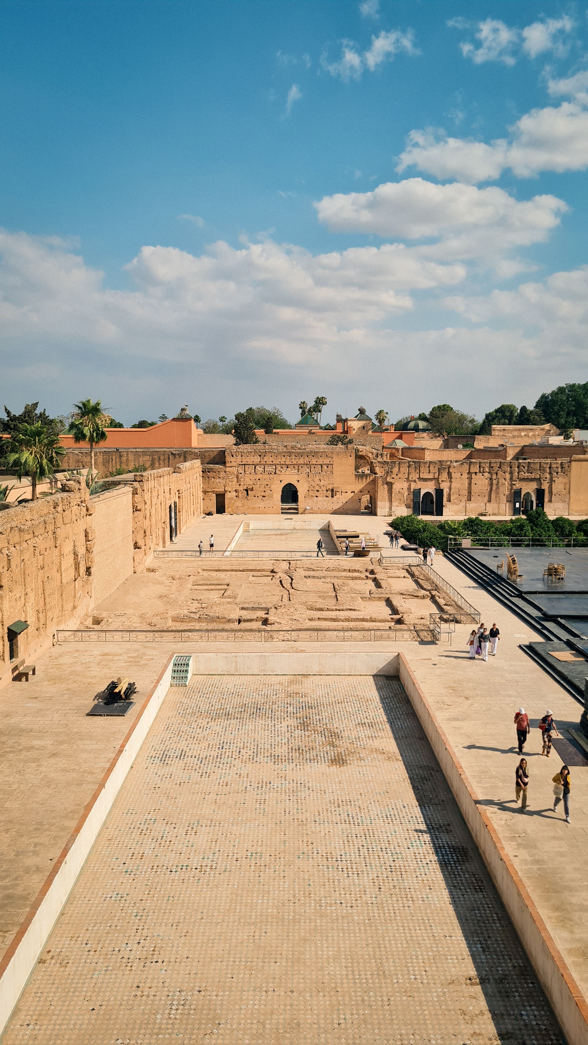 The ruined walls and sunken courtyard of El Badi Palace under a cloudy blue sky, Marrakech