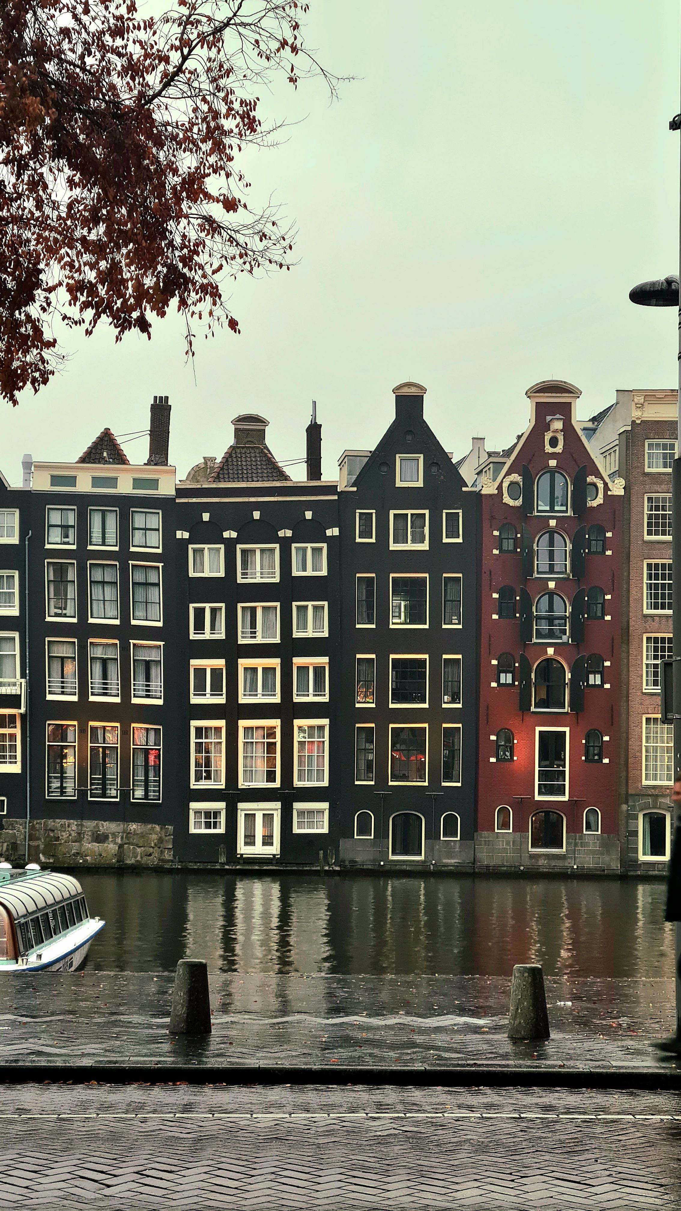 Dark and red gabled canal houses with cream window frames above a rainy canal, Amsterdam