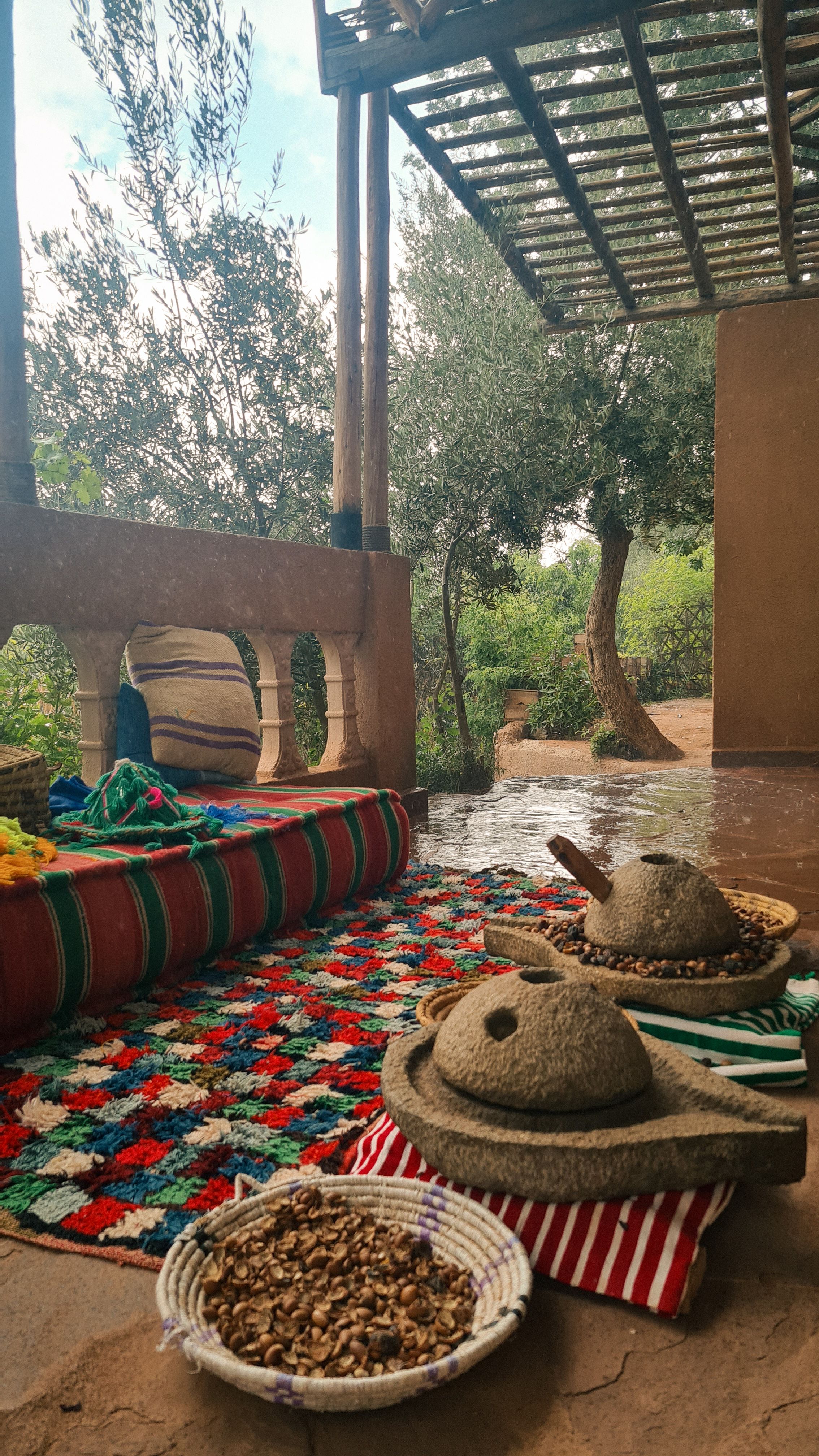 Two round stone grinding mills and a basket of nuts on a colorful woven rug on a terrace, Imlil