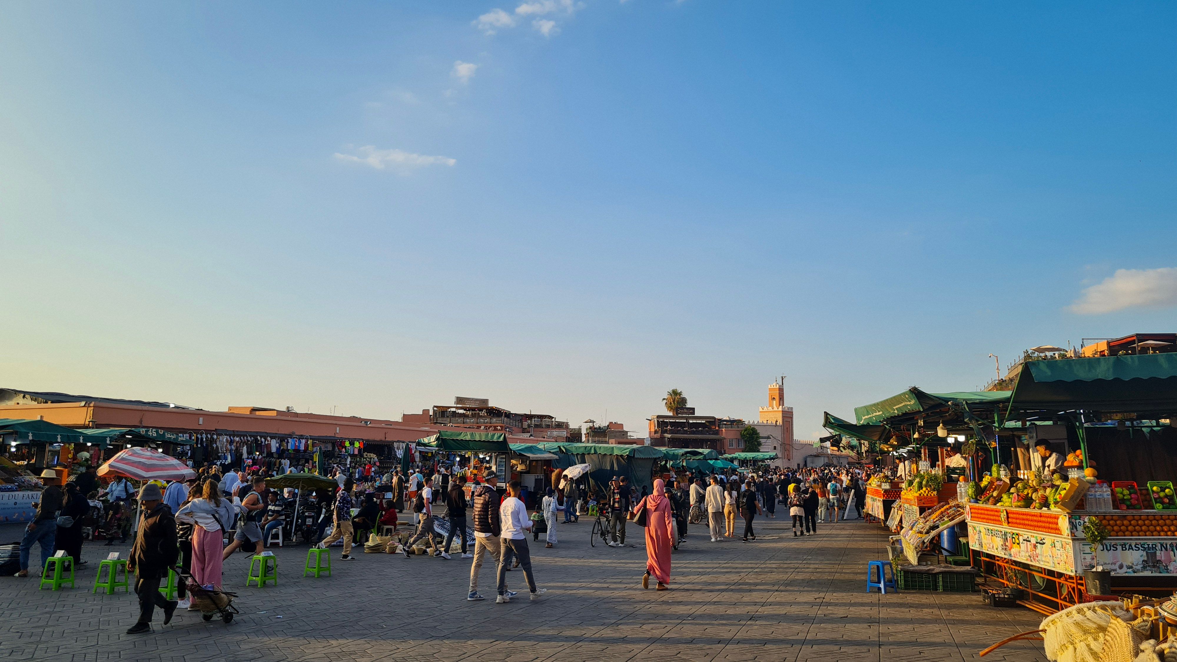 Crowds filling Jemaa el-Fnaa square at sunset, with food stalls on the right and the Koutoubia minaret in the distance, Marrakech