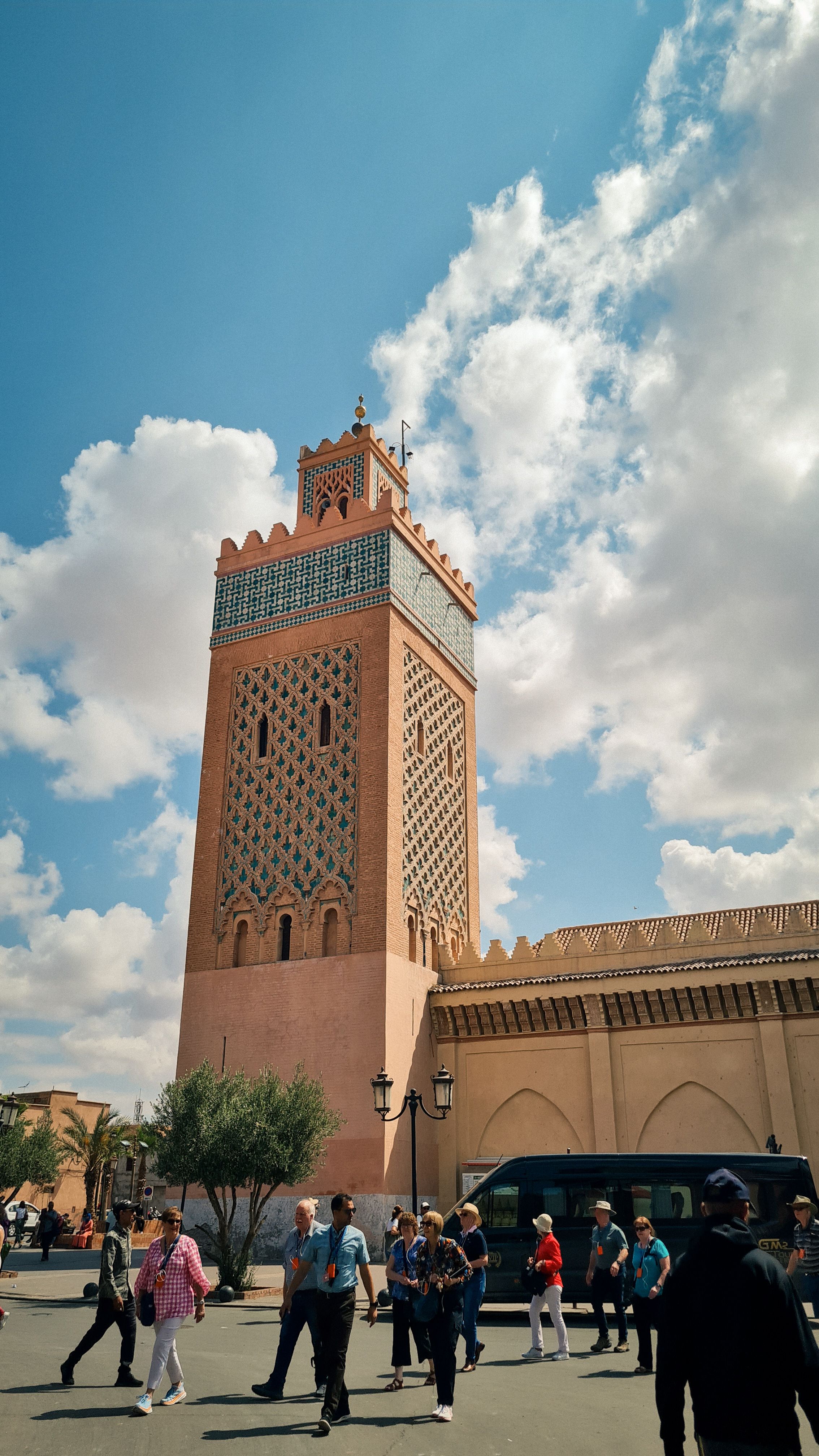 The tiled minaret of the Kasbah Mosque rising above a square with passing tourists, Marrakech