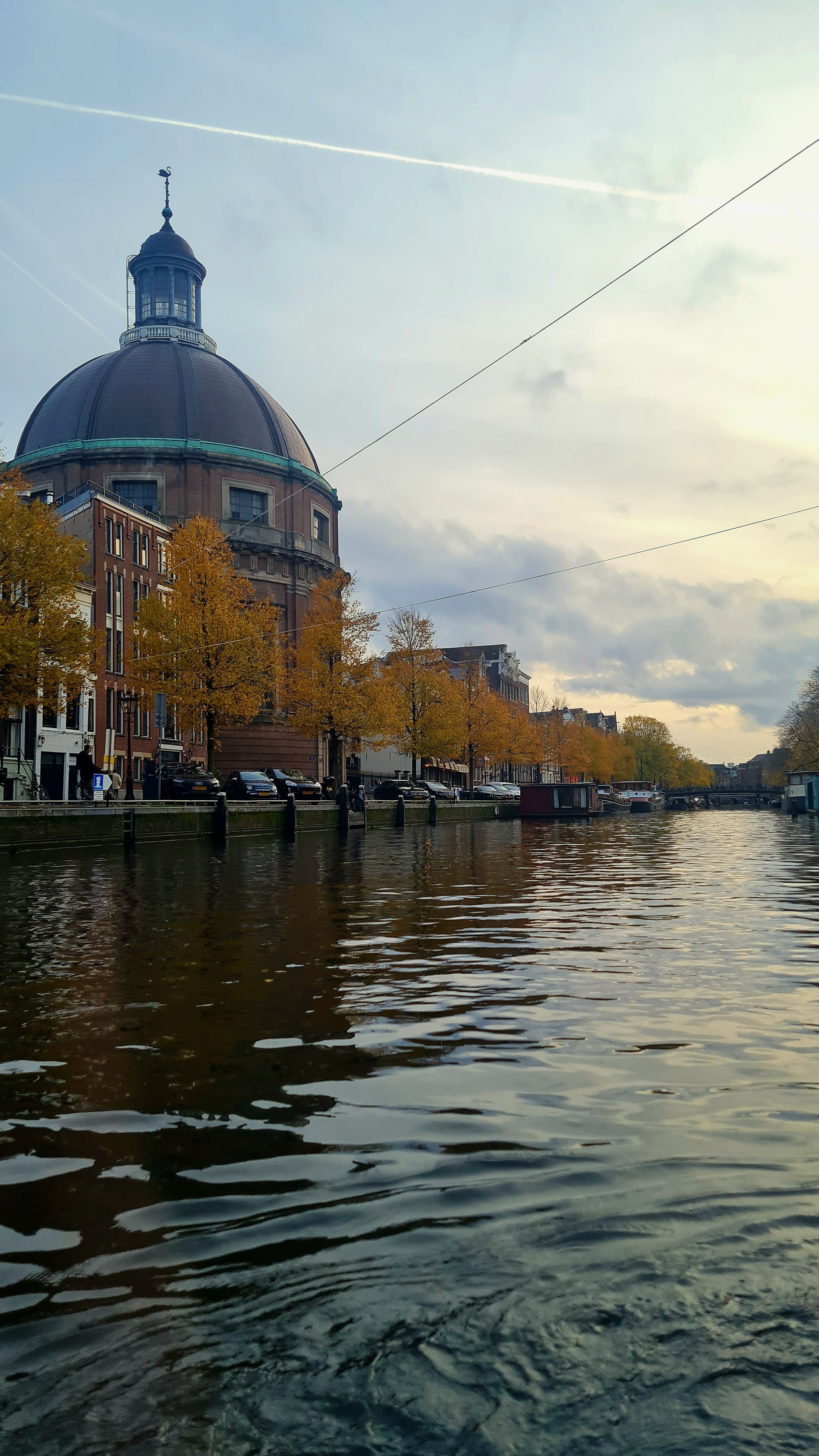 The green-trimmed dome of the Koepelkerk beside a canal lined with golden autumn trees and houseboats, Amsterdam