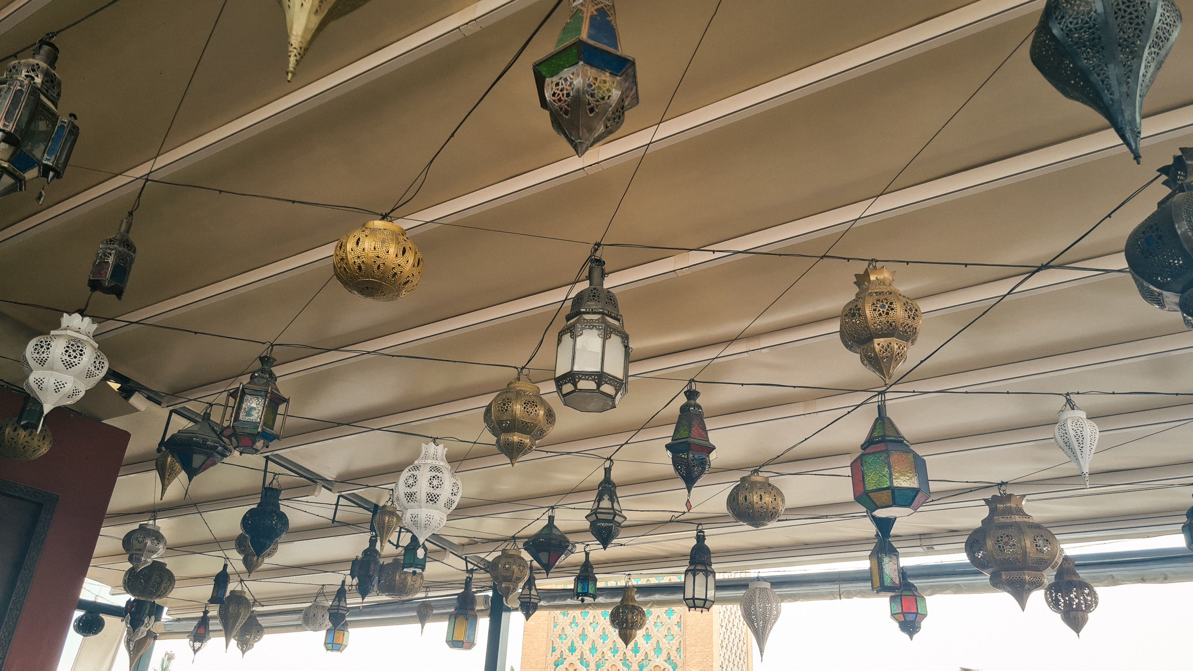 Dozens of colorful metal lanterns hanging from the ceiling of a rooftop terrace, Marrakech