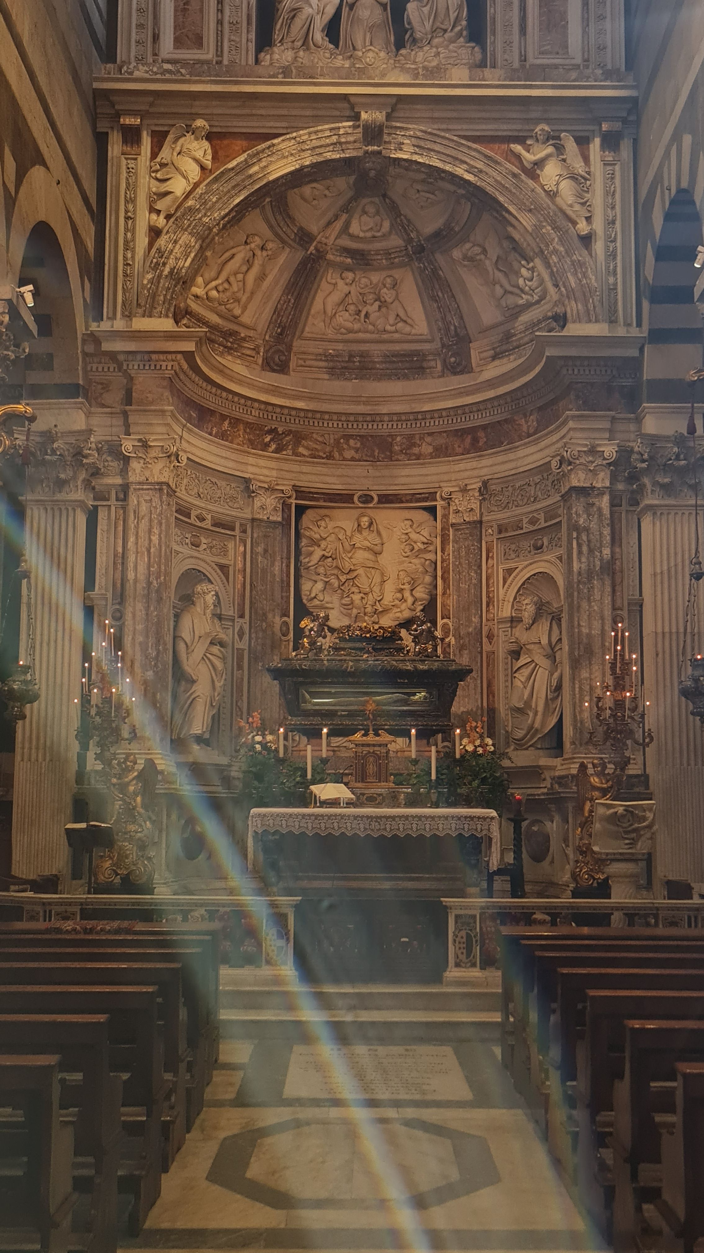 Side altar with marble reliefs and rows of wooden pews inside Pisa Cathedral
