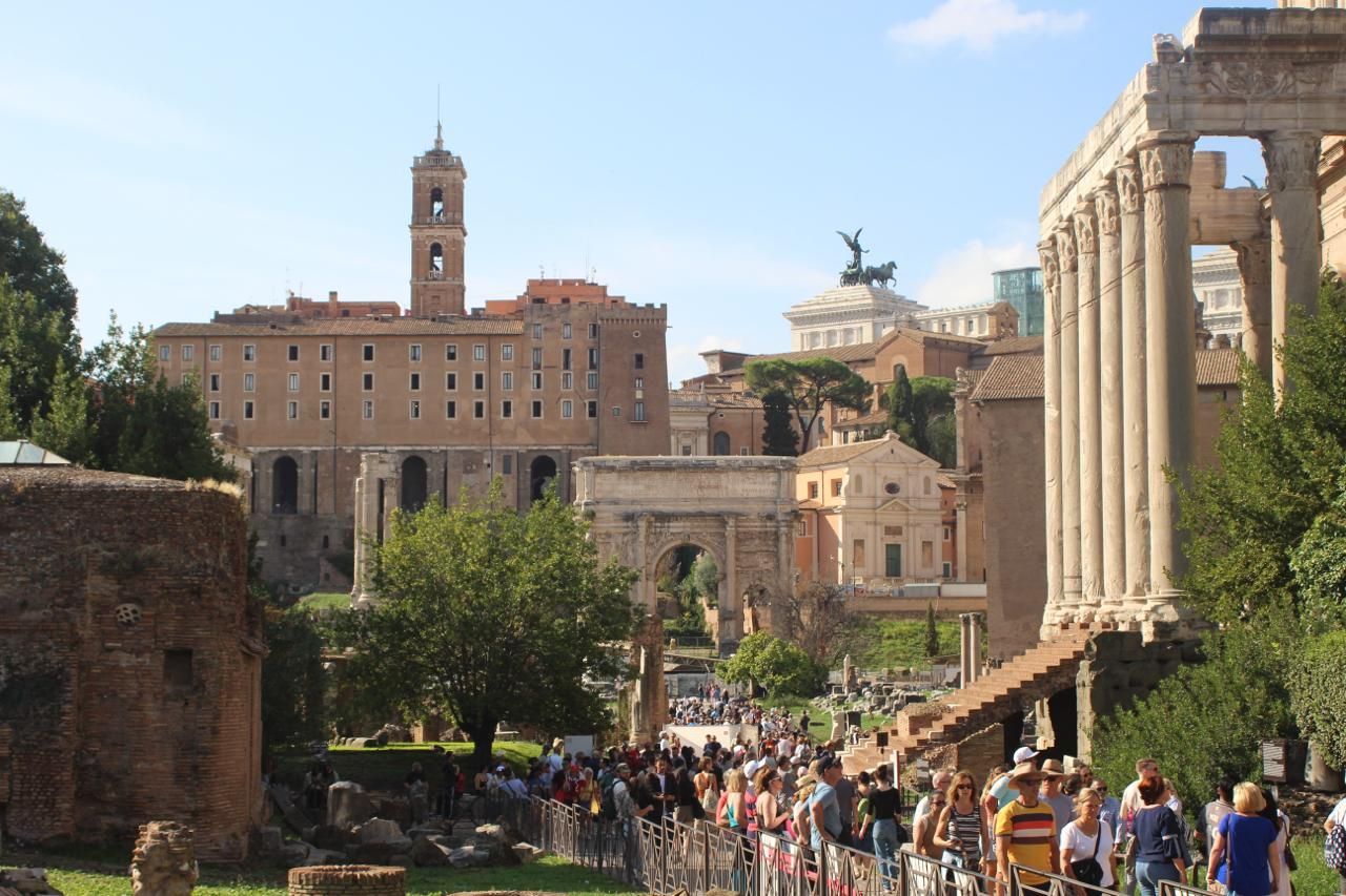 Crowd walking along the Roman Forum below an ancient arch and the Capitoline Hill, Rome