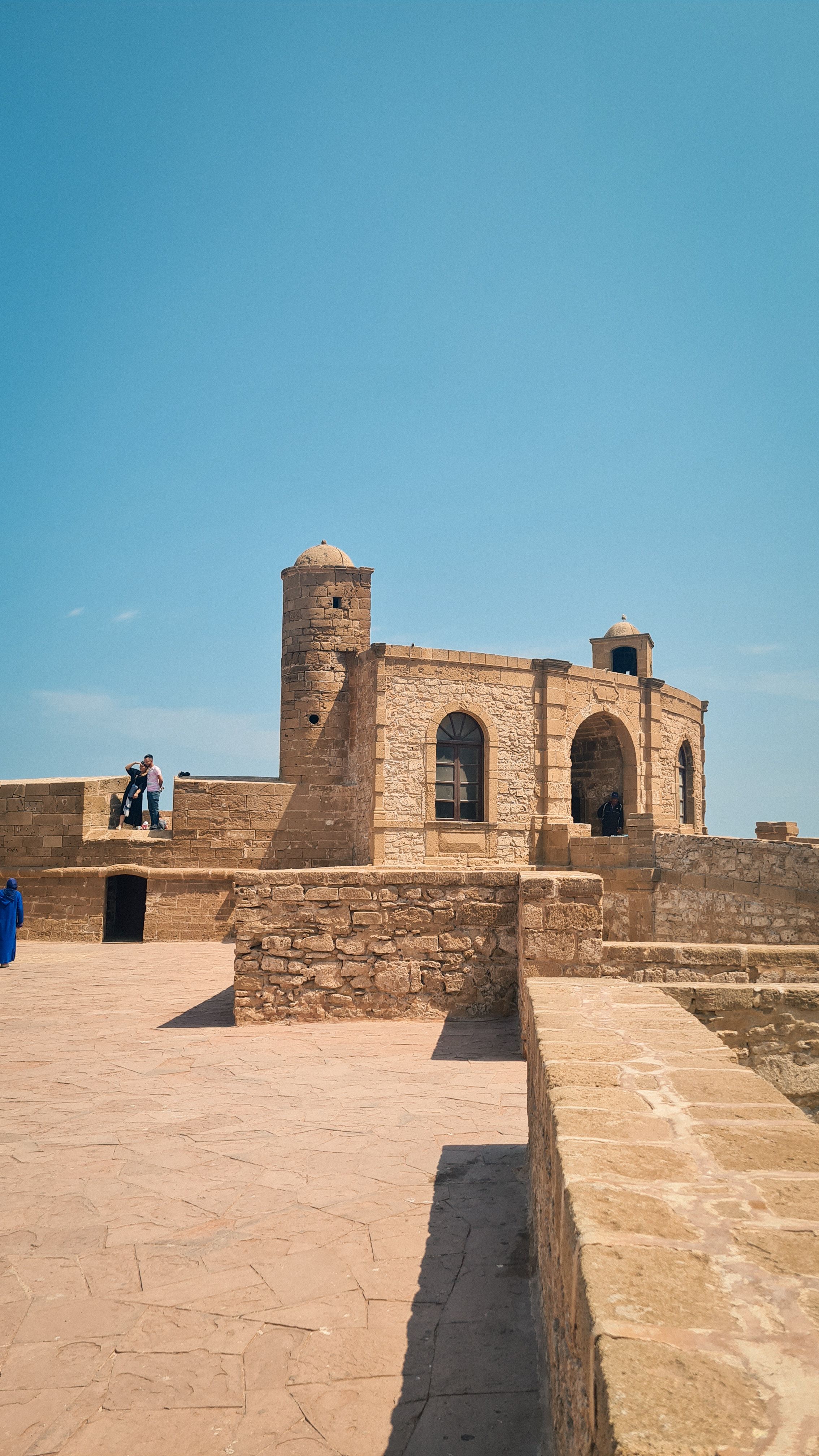 Sandstone ramparts and a round tower against a clear blue sky, Essaouira