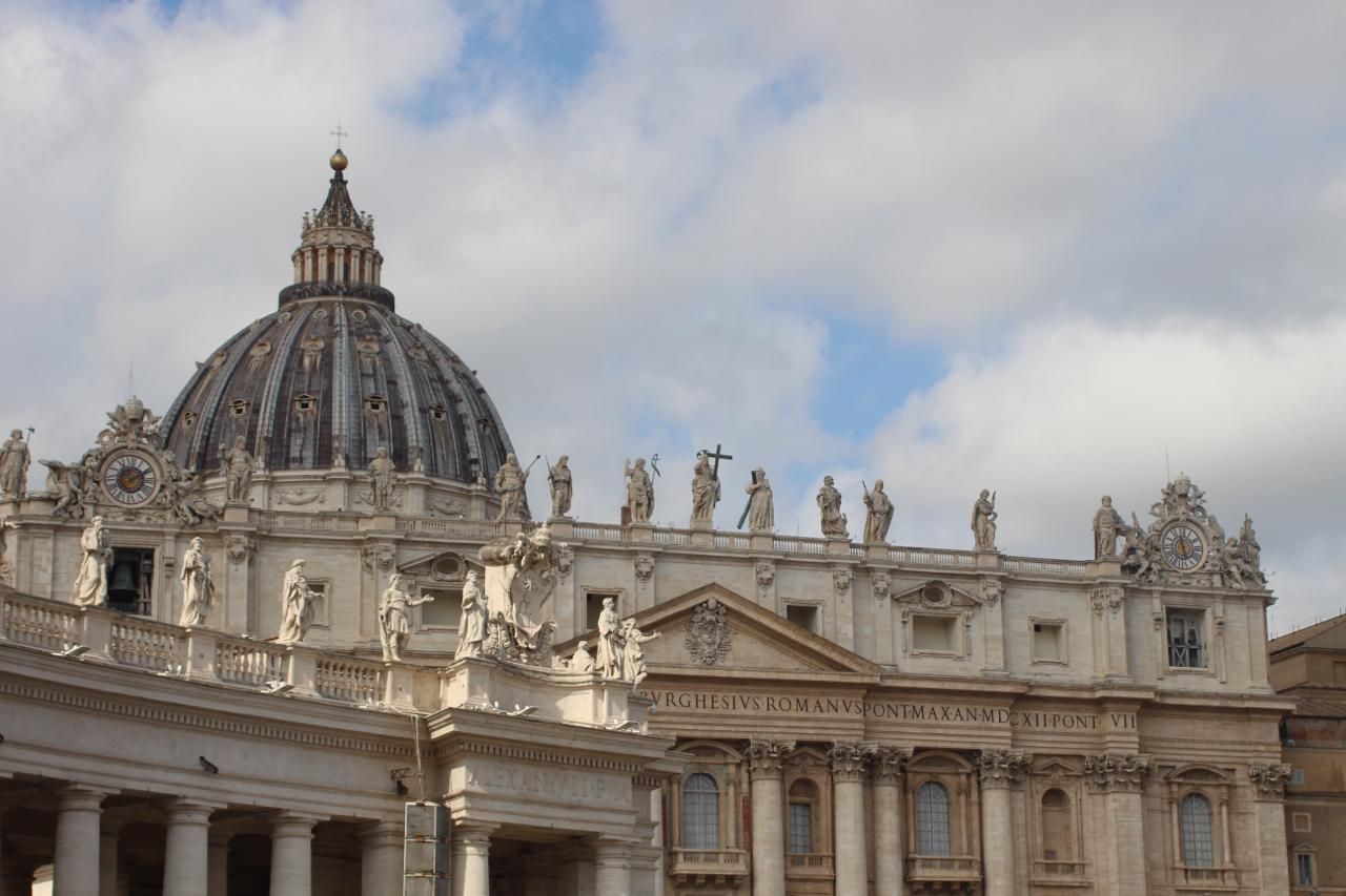 Dome and statue-topped facade of St. Peter's Basilica against a cloudy sky, Rome