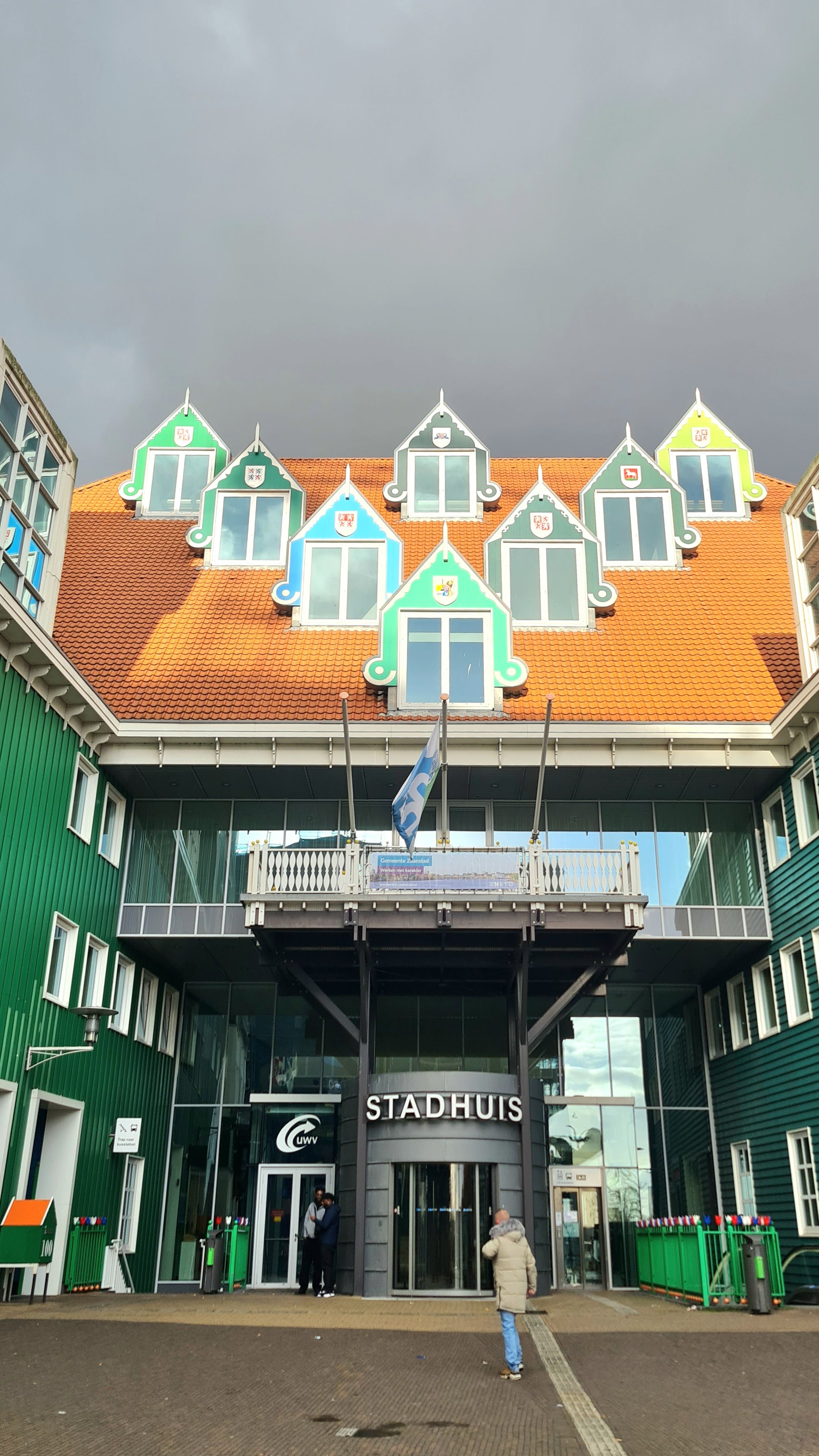 The Zaandam town hall entrance below an orange tiled roof with colorful green and blue gabled dormers under a dark sky, Zaandam