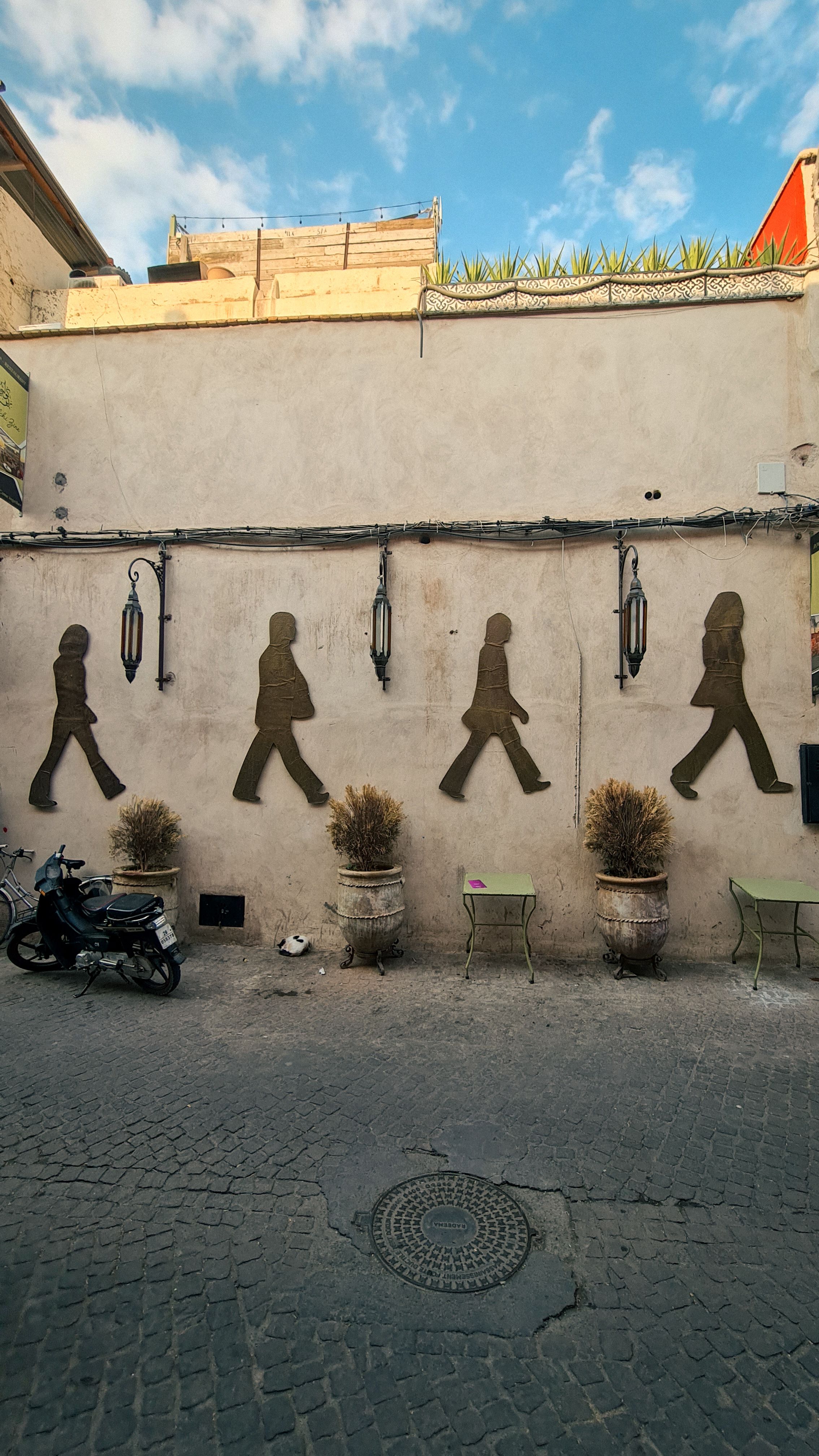 Four dark silhouettes of people walking in line painted on a pale wall above a cobbled street, Marrakech