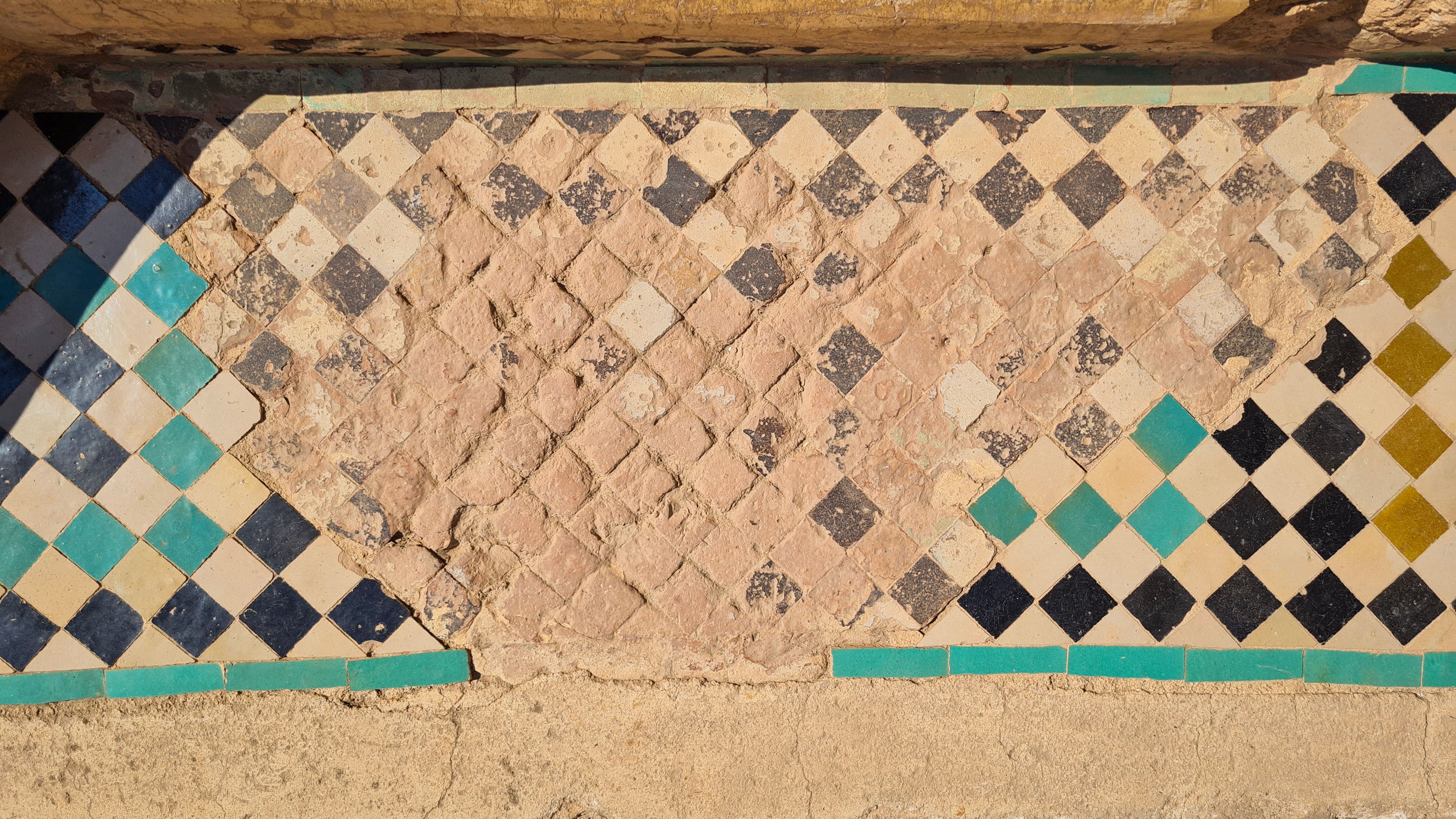 Worn black, white and turquoise zellige tiles with a patch of bare clay, Marrakech