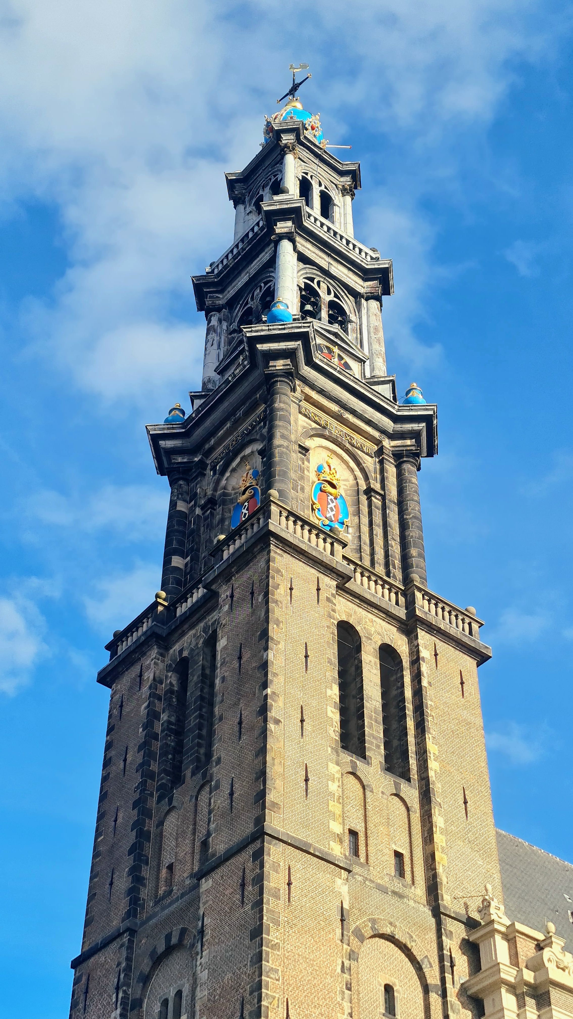 The ornate Westerkerk tower with its blue and gold crown and coats of arms against a blue sky, Amsterdam