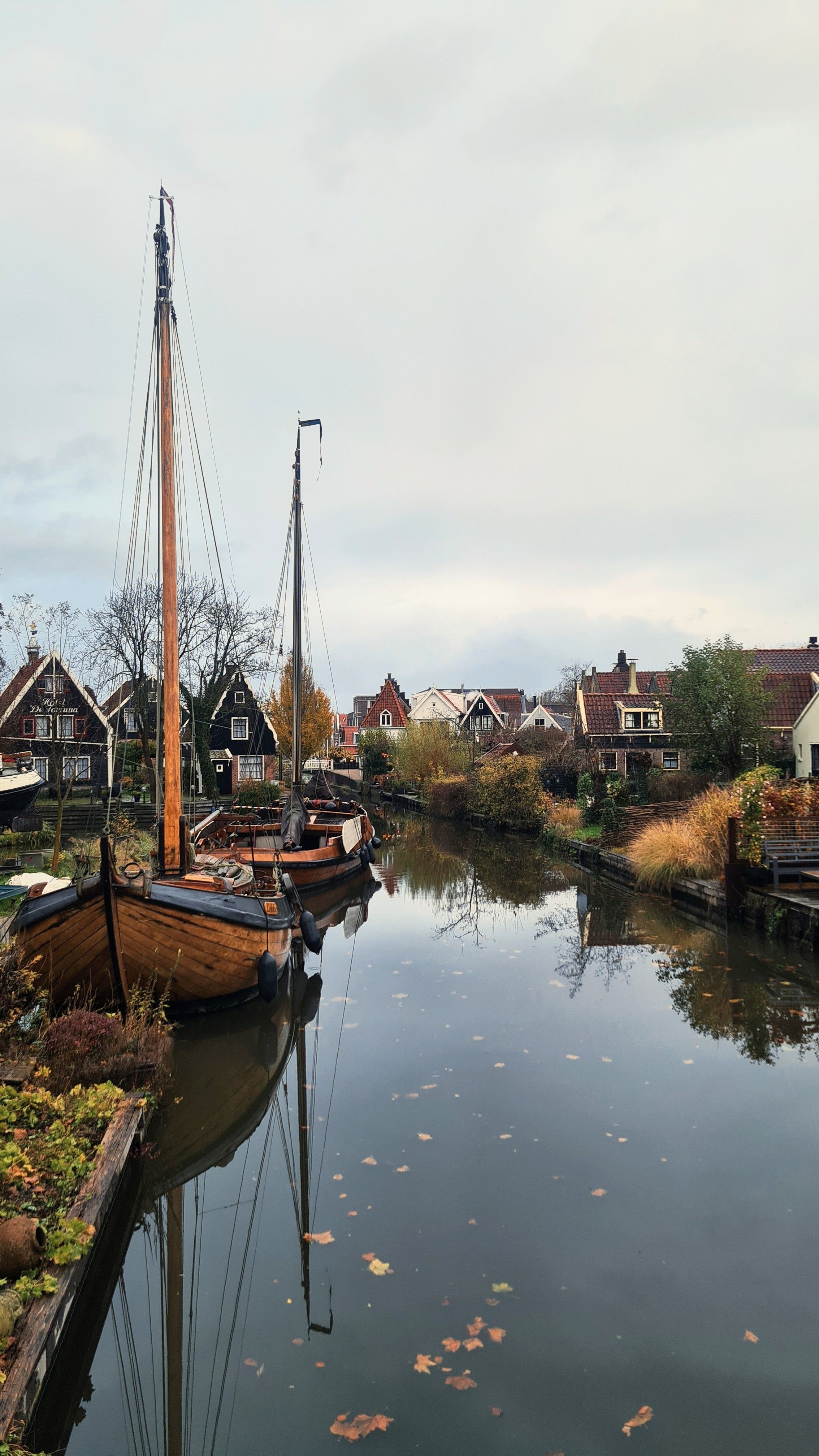 Two wooden sailing boats moored in a still canal reflecting masts and small gabled houses, Edam