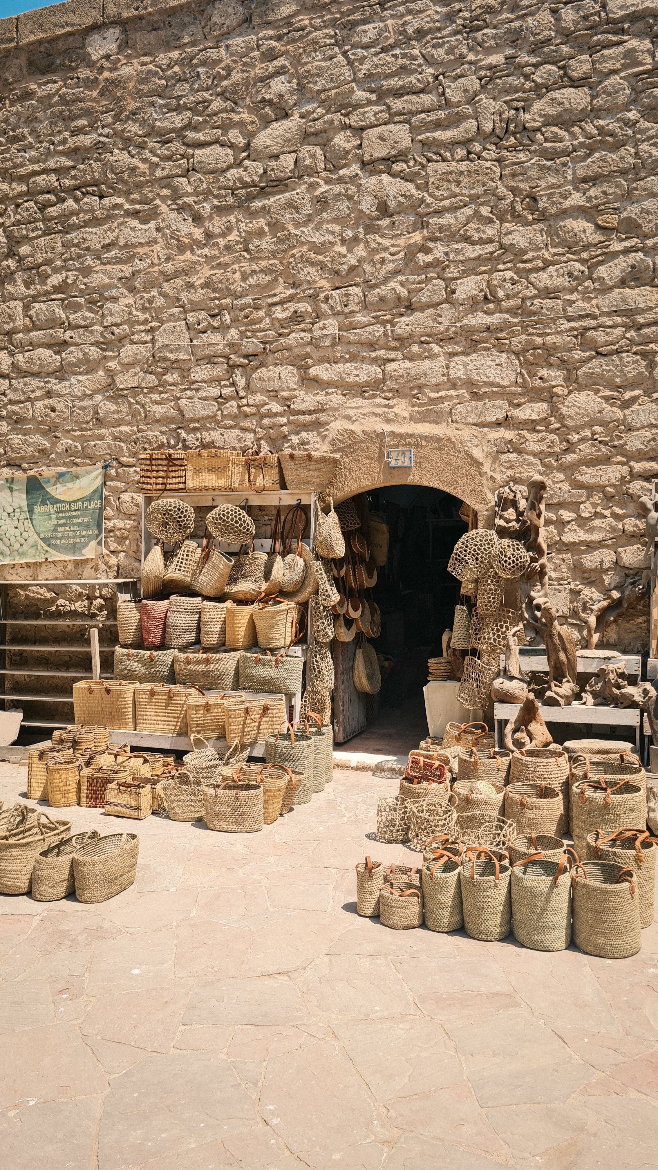 Woven baskets and straw bags stacked outside a doorway in a stone wall, Essaouira